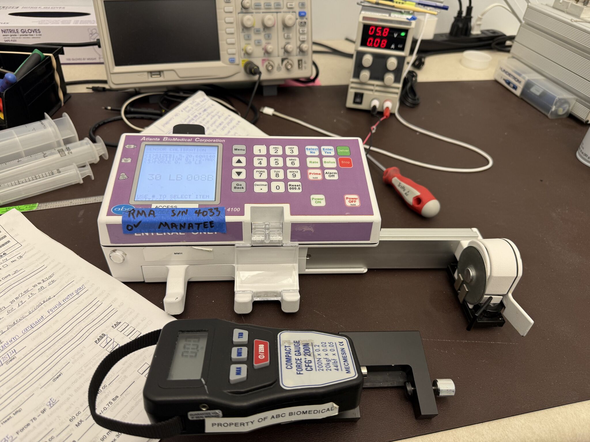 Enteral feeding pump on the repair bench with a force gauge for sensor calibration